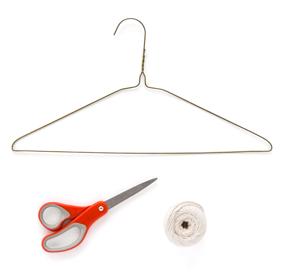 A top down image of a coat hanger, red scissors and a ball of string sitting on a white background.